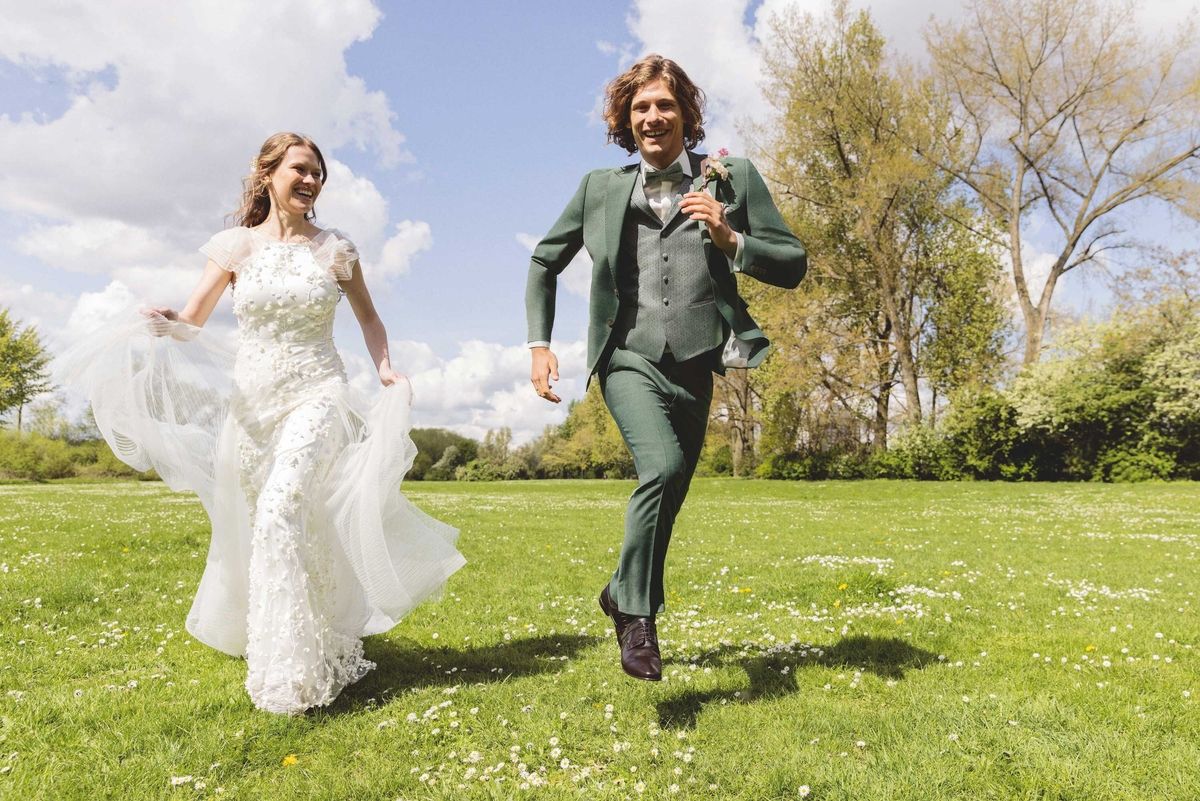 Braut und Bräutigam laufen fröhlich über eine mit Blumen übersäte Wiese.